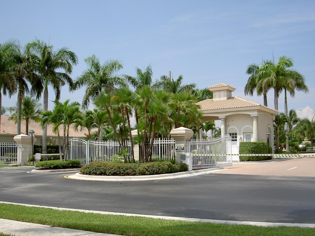 view of street featuring a gate, a gated entry, street lights, and curbs