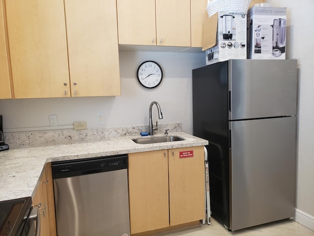 kitchen with light brown cabinets, stainless steel appliances, a sink, and light stone countertops