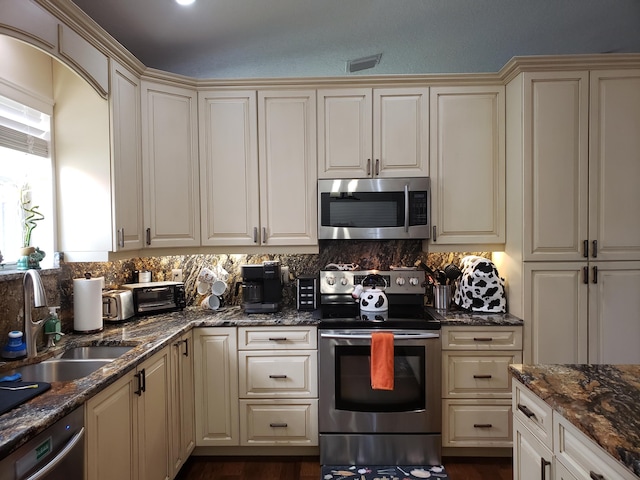 kitchen with backsplash, appliances with stainless steel finishes, dark stone counters, and a sink