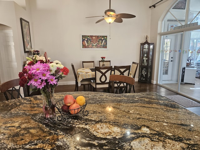 dining area with dark wood-type flooring, arched walkways, a high ceiling, and baseboards