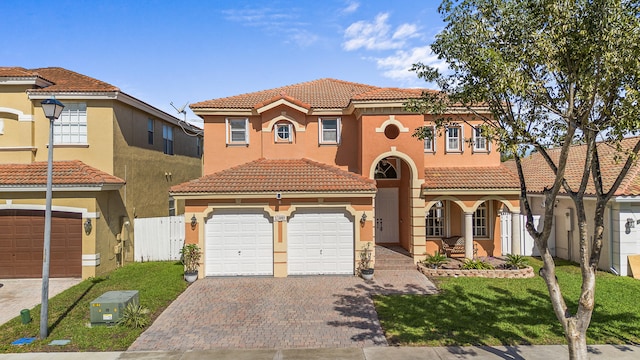 mediterranean / spanish house with decorative driveway, fence, an attached garage, and stucco siding