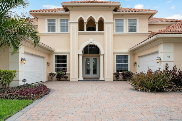 property entrance with stucco siding, french doors, a garage, a tiled roof, and decorative driveway