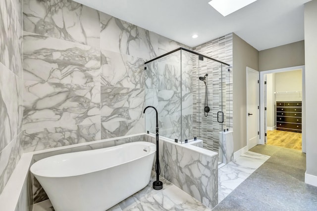 bathroom featuring stone wall, a freestanding tub, a walk in closet, and a marble finish shower