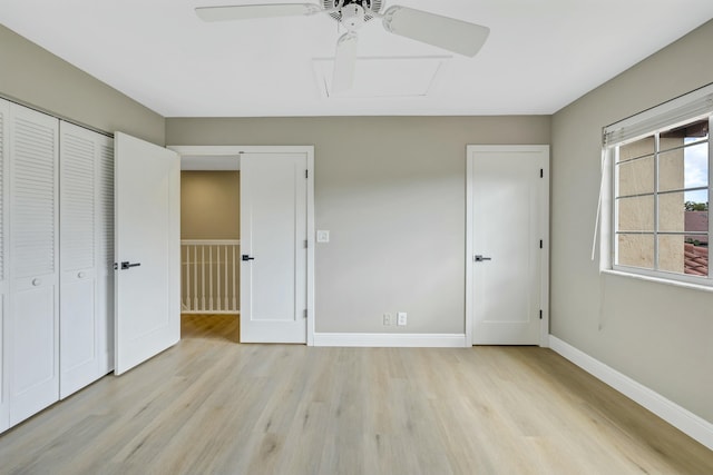 unfurnished bedroom featuring a closet, light wood-style flooring, attic access, ceiling fan, and baseboards