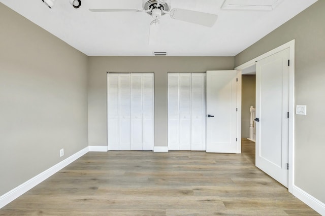 unfurnished bedroom with a ceiling fan, visible vents, baseboards, light wood-type flooring, and two closets