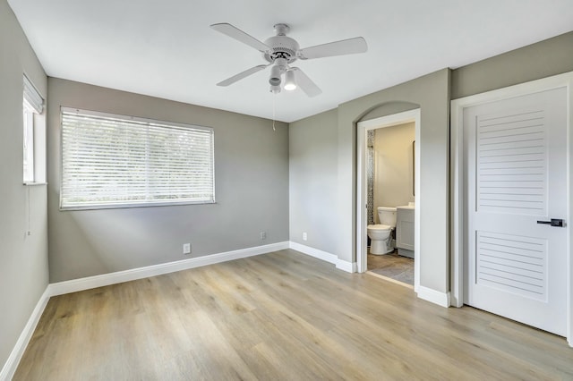 unfurnished bedroom with light wood-style flooring, baseboards, ceiling fan, and connected bathroom