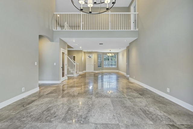 unfurnished living room with a notable chandelier, a towering ceiling, and baseboards