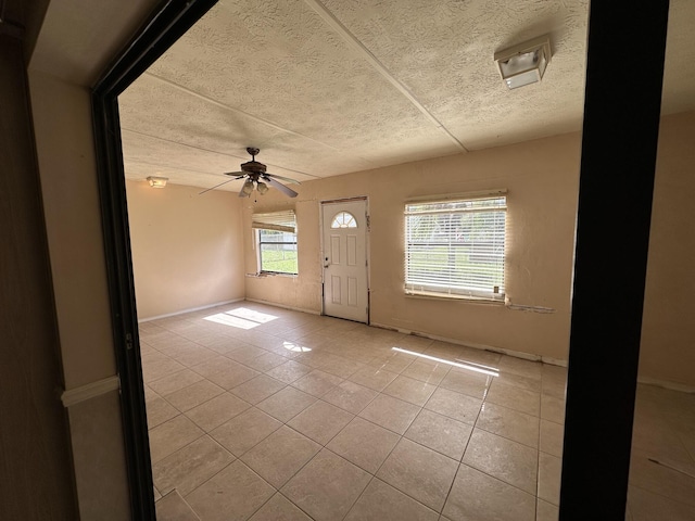 entryway with a ceiling fan, a textured ceiling, baseboards, and light tile patterned floors