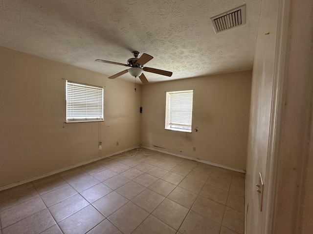 spare room featuring light tile patterned floors, a textured ceiling, visible vents, baseboards, and a ceiling fan