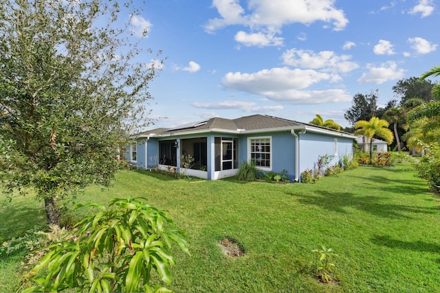 rear view of property with stucco siding, roof mounted solar panels, a sunroom, and a yard