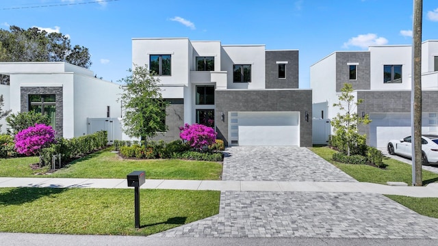 modern home featuring a front yard, an attached garage, decorative driveway, and stucco siding