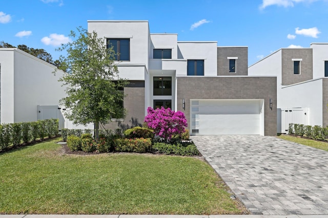 modern home featuring an attached garage, a front lawn, stucco siding, and decorative driveway