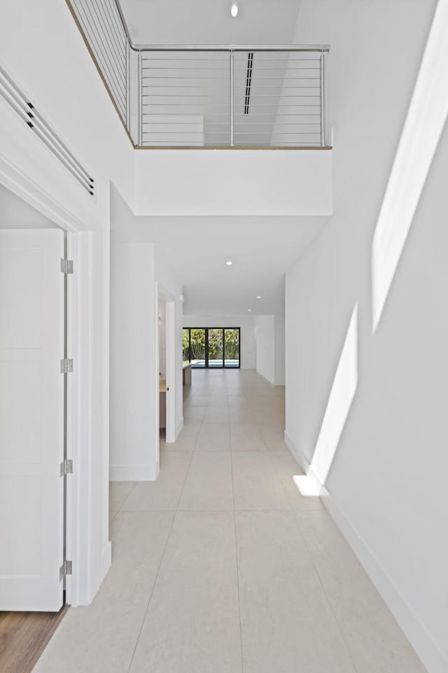 corridor featuring tile patterned floors, a towering ceiling, and baseboards