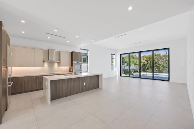 kitchen featuring open floor plan, modern cabinets, wall chimney range hood, light countertops, and appliances with stainless steel finishes