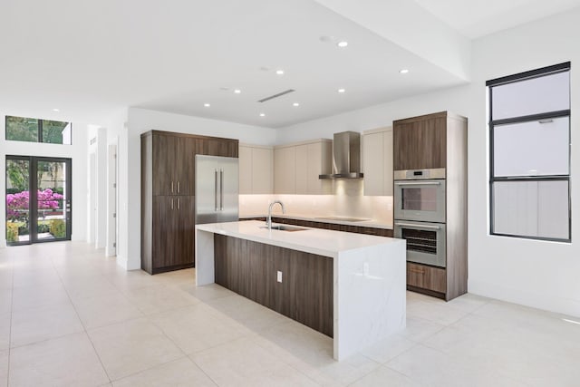 kitchen featuring a sink, stainless steel double oven, modern cabinets, black electric stovetop, and wall chimney exhaust hood