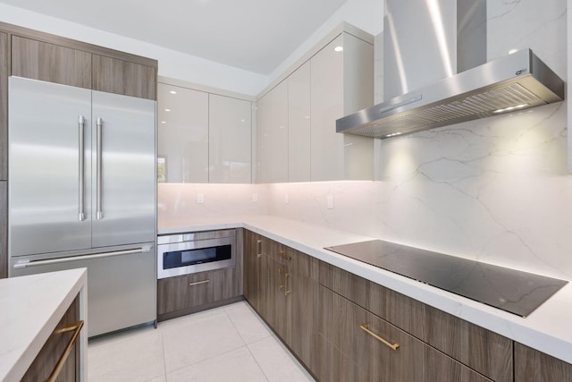 kitchen featuring wall chimney exhaust hood, modern cabinets, tasteful backsplash, built in fridge, and black electric cooktop