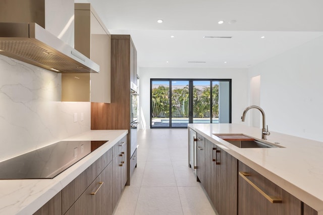 kitchen with a sink, modern cabinets, light stone counters, wall chimney range hood, and black electric stovetop
