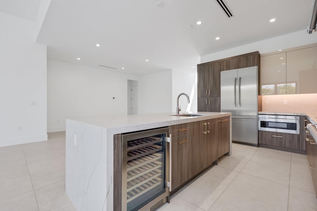 kitchen with a sink, a large island with sink, modern cabinets, stainless steel built in refrigerator, and wine cooler