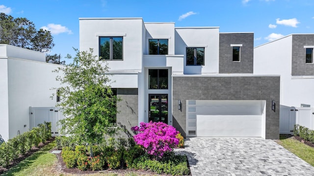 contemporary house featuring a garage, decorative driveway, stucco siding, and fence