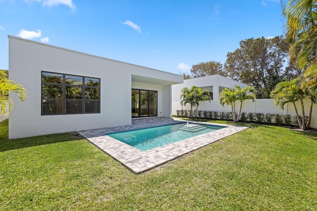 rear view of property featuring fence, a fenced in pool, a lawn, and stucco siding