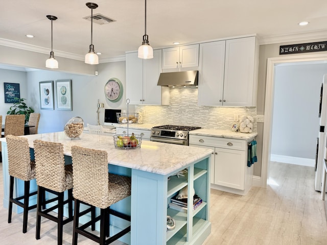 kitchen with stainless steel gas range oven, light wood-type flooring, ornamental molding, under cabinet range hood, and tasteful backsplash