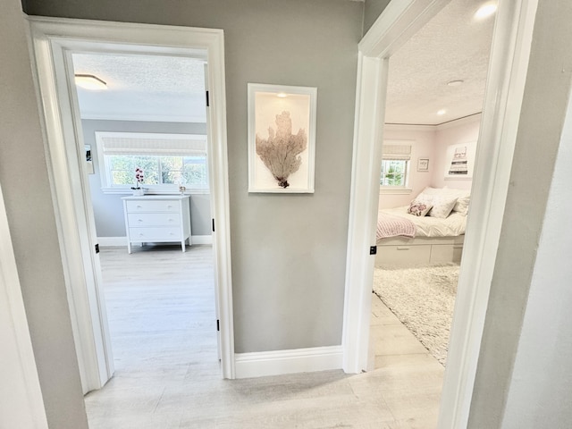 hall featuring ornamental molding, wood finished floors, baseboards, and a textured ceiling