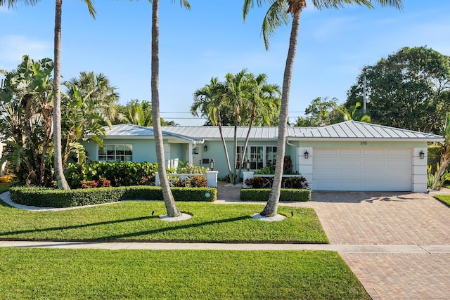 single story home with a front yard, stucco siding, metal roof, decorative driveway, and an attached garage