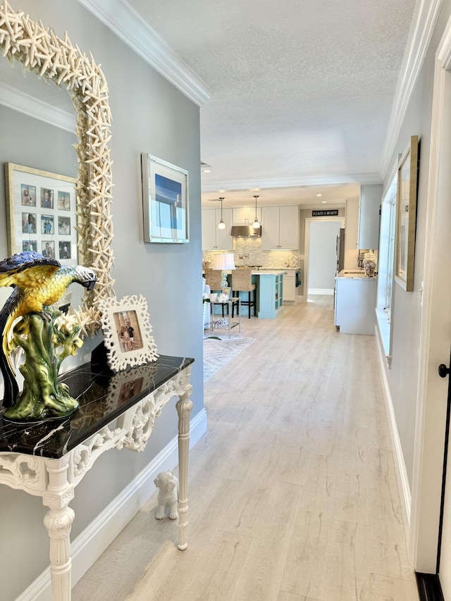 hallway featuring baseboards, a textured ceiling, crown molding, and light wood finished floors