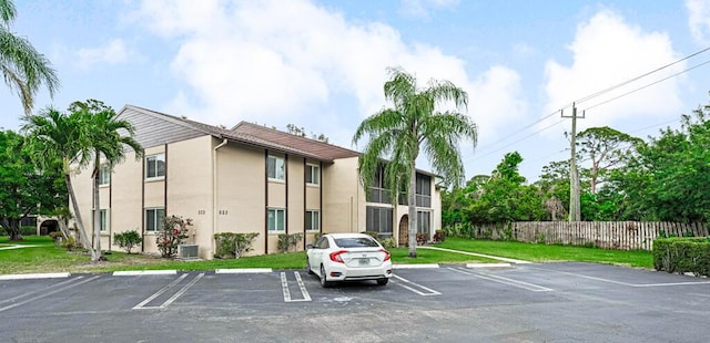 view of property with central air condition unit, uncovered parking, and fence