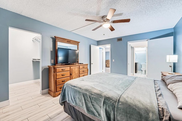 bedroom with a walk in closet, a closet, visible vents, light wood-style flooring, and baseboards