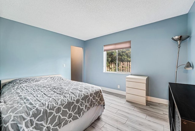 bedroom featuring wood finish floors, a textured ceiling, and baseboards