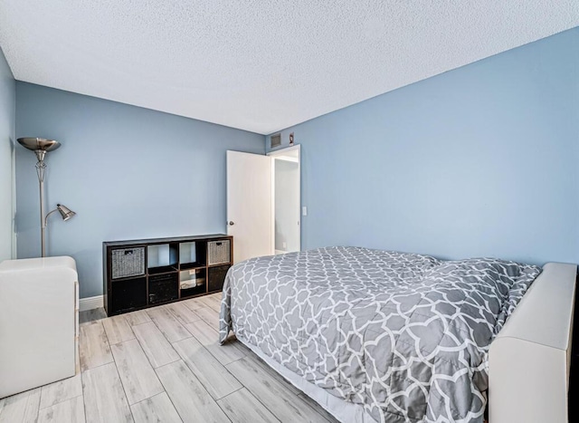 bedroom featuring a textured ceiling, baseboards, and wood tiled floor