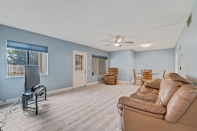 living area with a textured ceiling, ceiling fan, light wood-type flooring, and baseboards