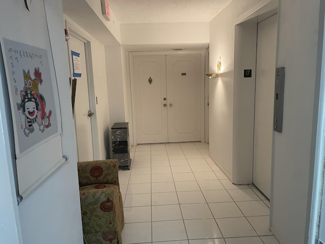 corridor with light tile patterned floors, elevator, and a textured ceiling