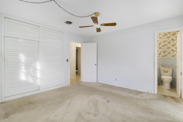 unfurnished bedroom featuring light colored carpet, a wainscoted wall, tile walls, visible vents, and ensuite bath