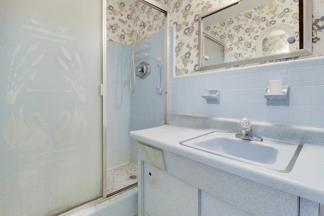 full bath with a wainscoted wall, tile walls, a shower stall, vanity, and wallpapered walls