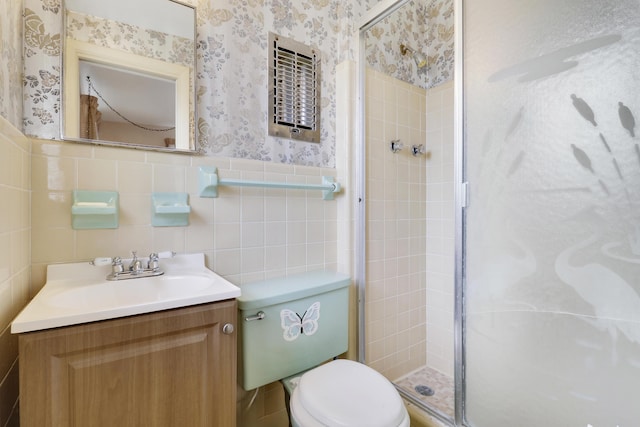 bathroom with wallpapered walls, wainscoting, toilet, vanity, and a shower stall