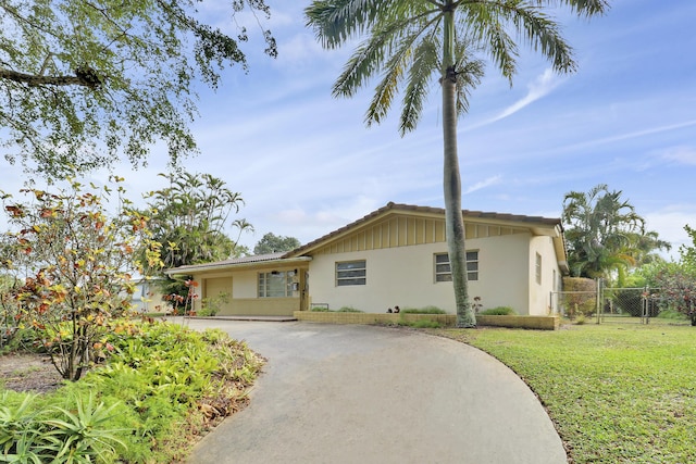 ranch-style home featuring driveway, stucco siding, fence, and a front yard