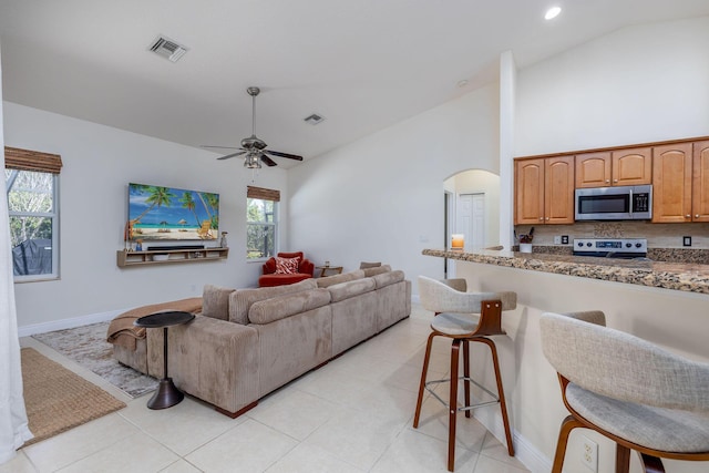 living area featuring arched walkways, visible vents, high vaulted ceiling, and light tile patterned floors