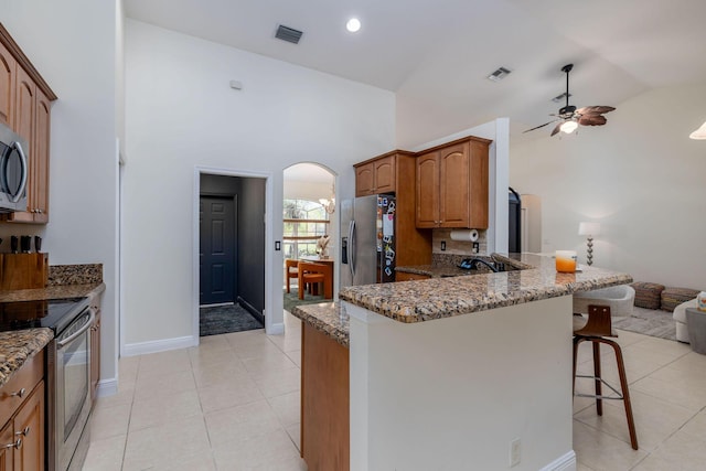 kitchen featuring light stone counters, visible vents, arched walkways, stainless steel appliances, and a kitchen bar