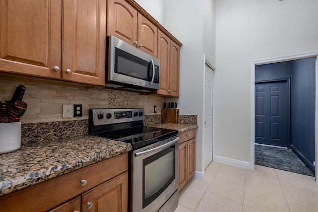 kitchen featuring light tile patterned flooring, dark stone countertops, stainless steel appliances, and brown cabinetry