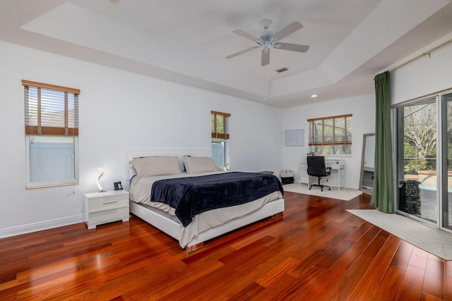 bedroom with visible vents, a tray ceiling, wood-type flooring, baseboards, and access to exterior