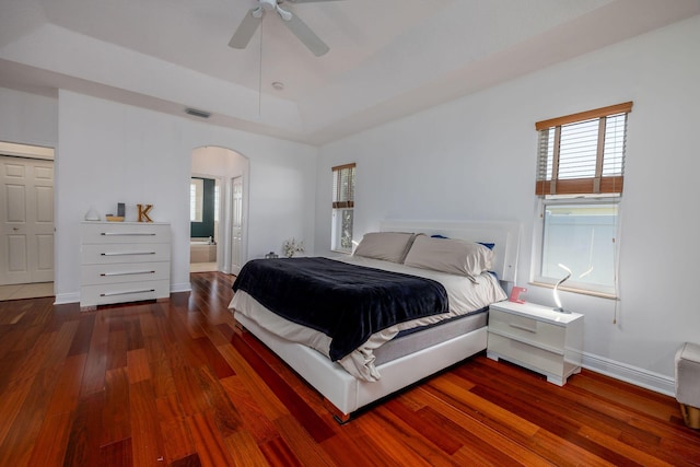 bedroom with visible vents, wood finished floors, baseboards, arched walkways, and a raised ceiling