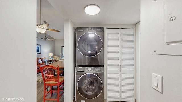 clothes washing area featuring a ceiling fan, stacked washer / dryer, laundry area, and wood finished floors