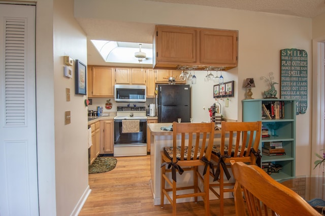 kitchen featuring white electric range, light wood-style floors, light countertops, freestanding refrigerator, and stainless steel microwave