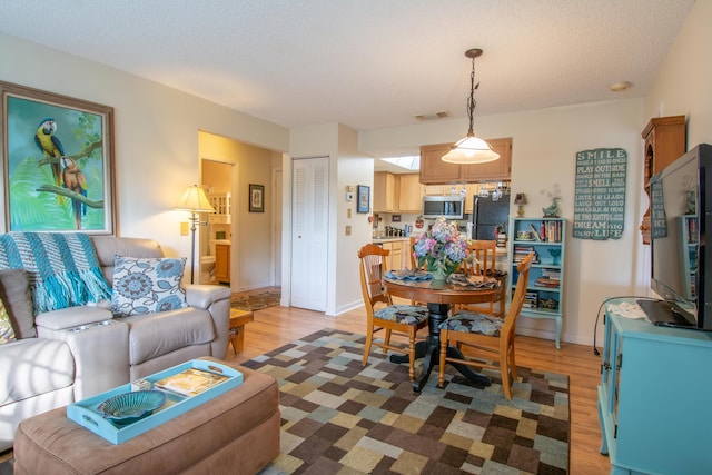 living room with visible vents, a textured ceiling, baseboards, and wood finished floors