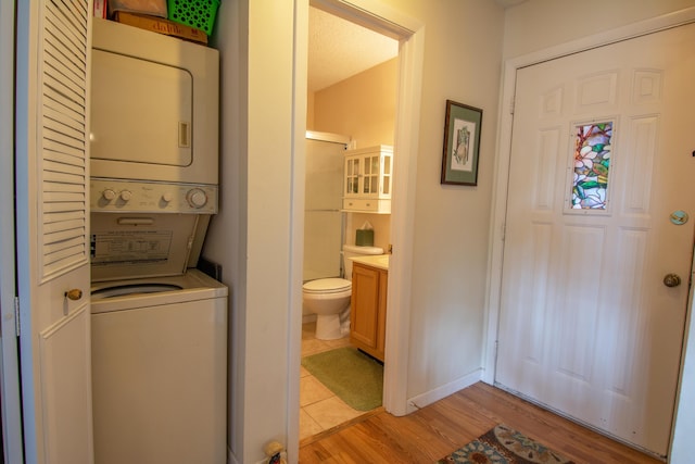 clothes washing area with light wood-type flooring, stacked washer / drying machine, laundry area, and baseboards