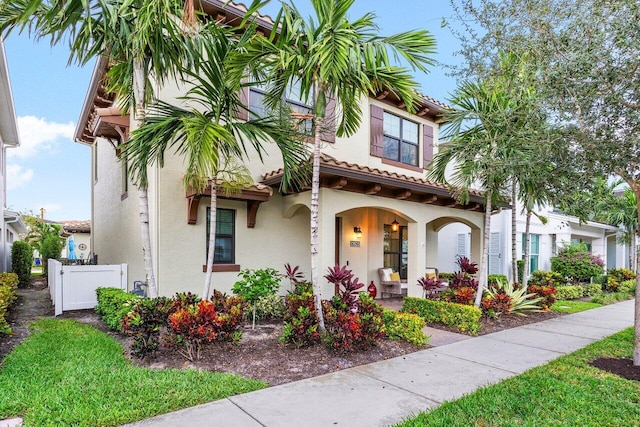 view of front of house with a porch, a tile roof, fence, and stucco siding