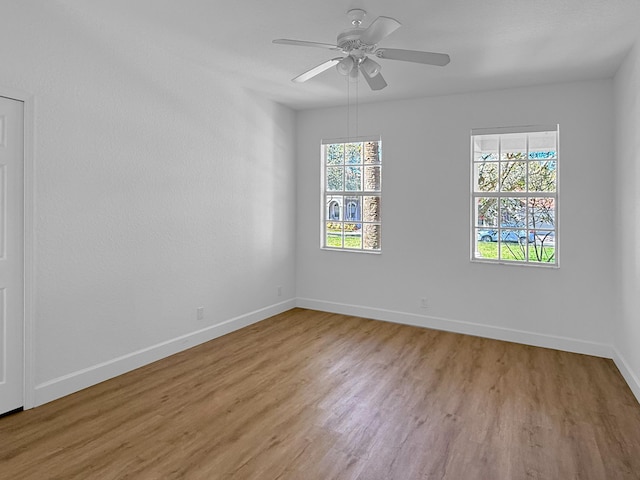 empty room with plenty of natural light, light wood finished floors, baseboards, and ceiling fan