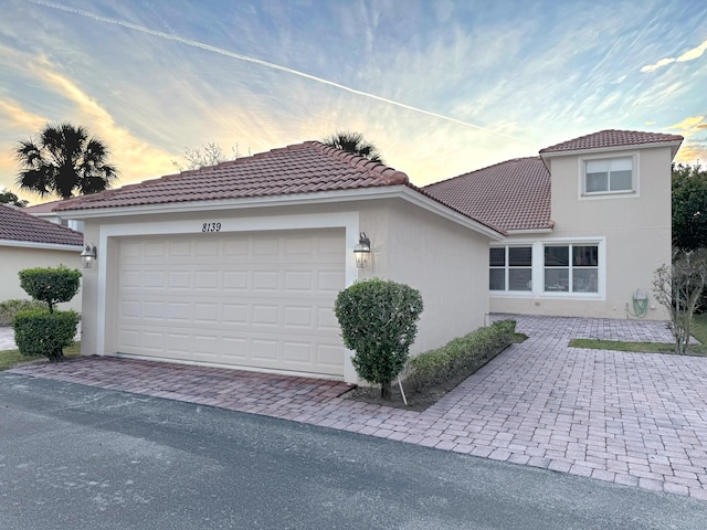 view of front of home featuring a garage, a tiled roof, driveway, and stucco siding